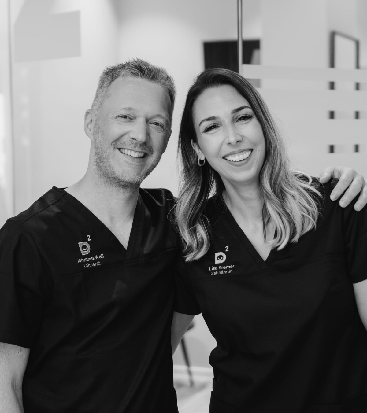 Johannes Well (links) und Lisa Kremer (rechts) lachend mit Arm über der Schulter.